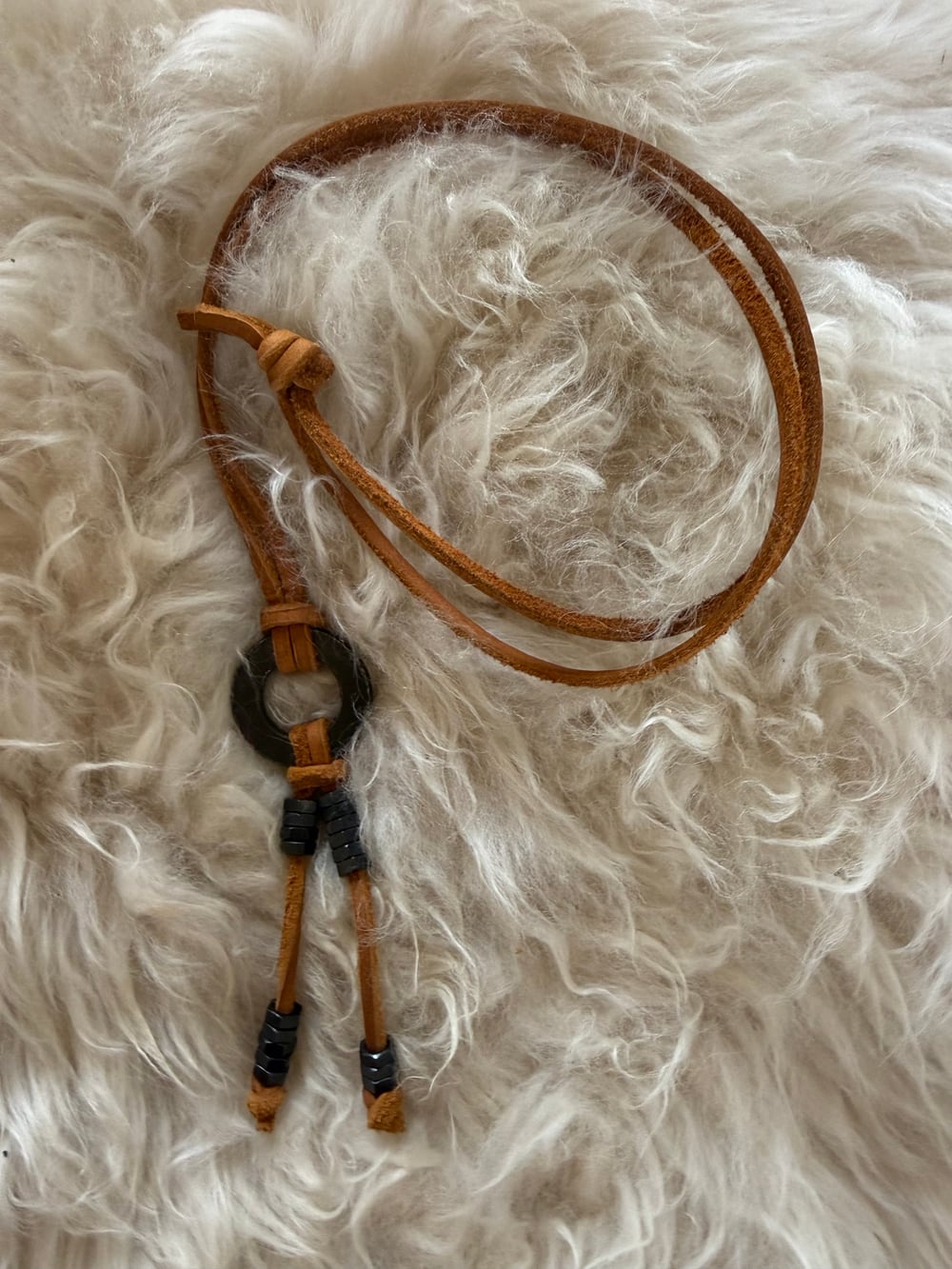 Close view of the black necklace on sheepskin, with the black hex nuts slid to different places along the two leather strands.