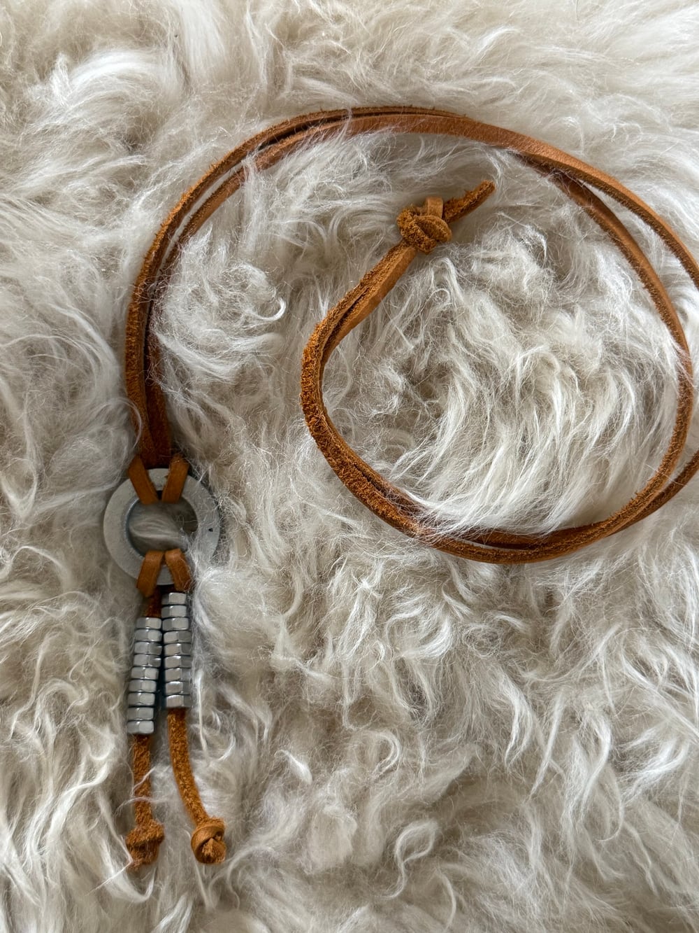 The silver necklace resting on cream sheepskin, showing the full length of the leather strap and the knot that closes it.